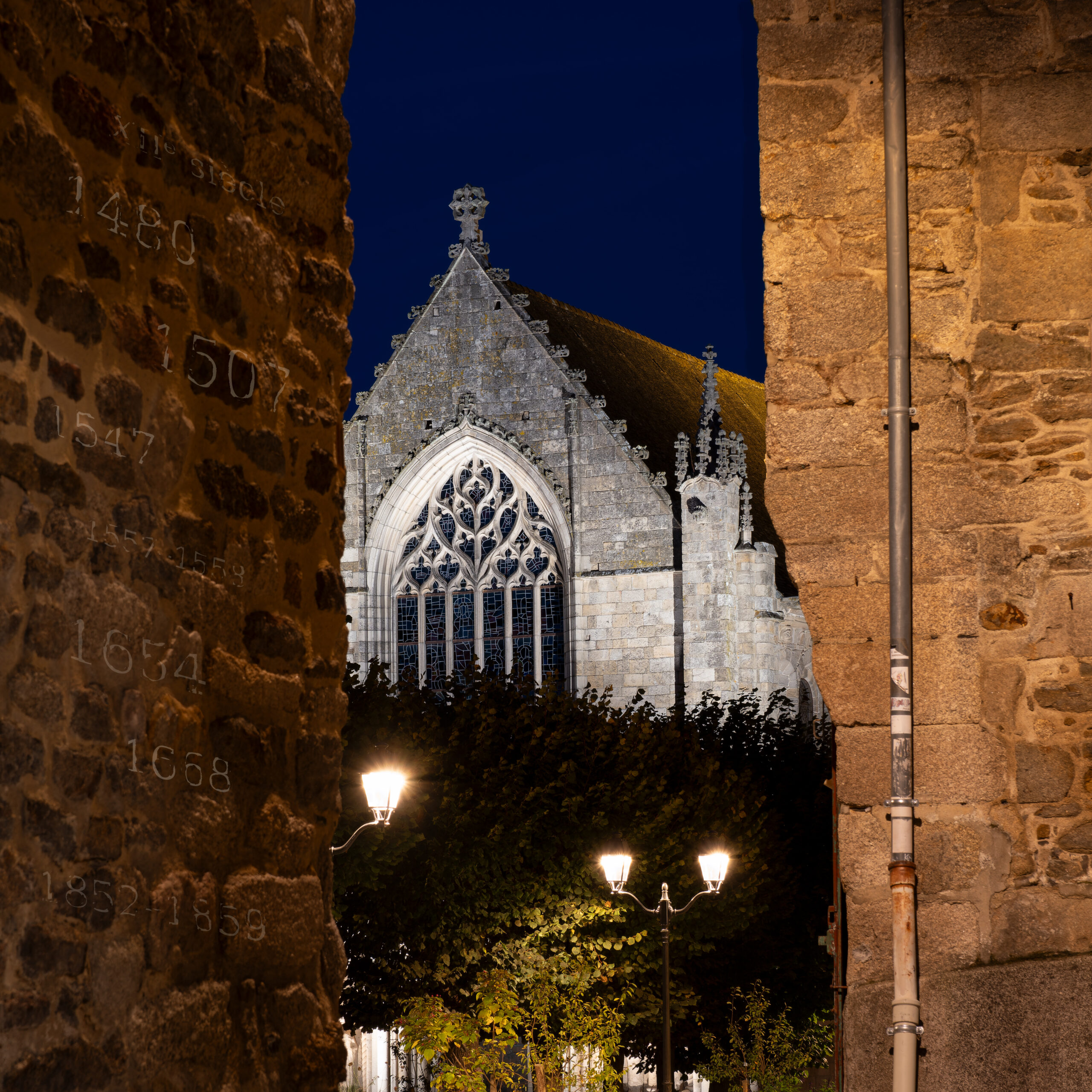 La basilique Saint-Sauveur de Dinan entre deux murs, avec des dates patinées sur le mur de gauche.